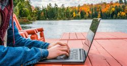 Person working on laptop beside lake during the fall